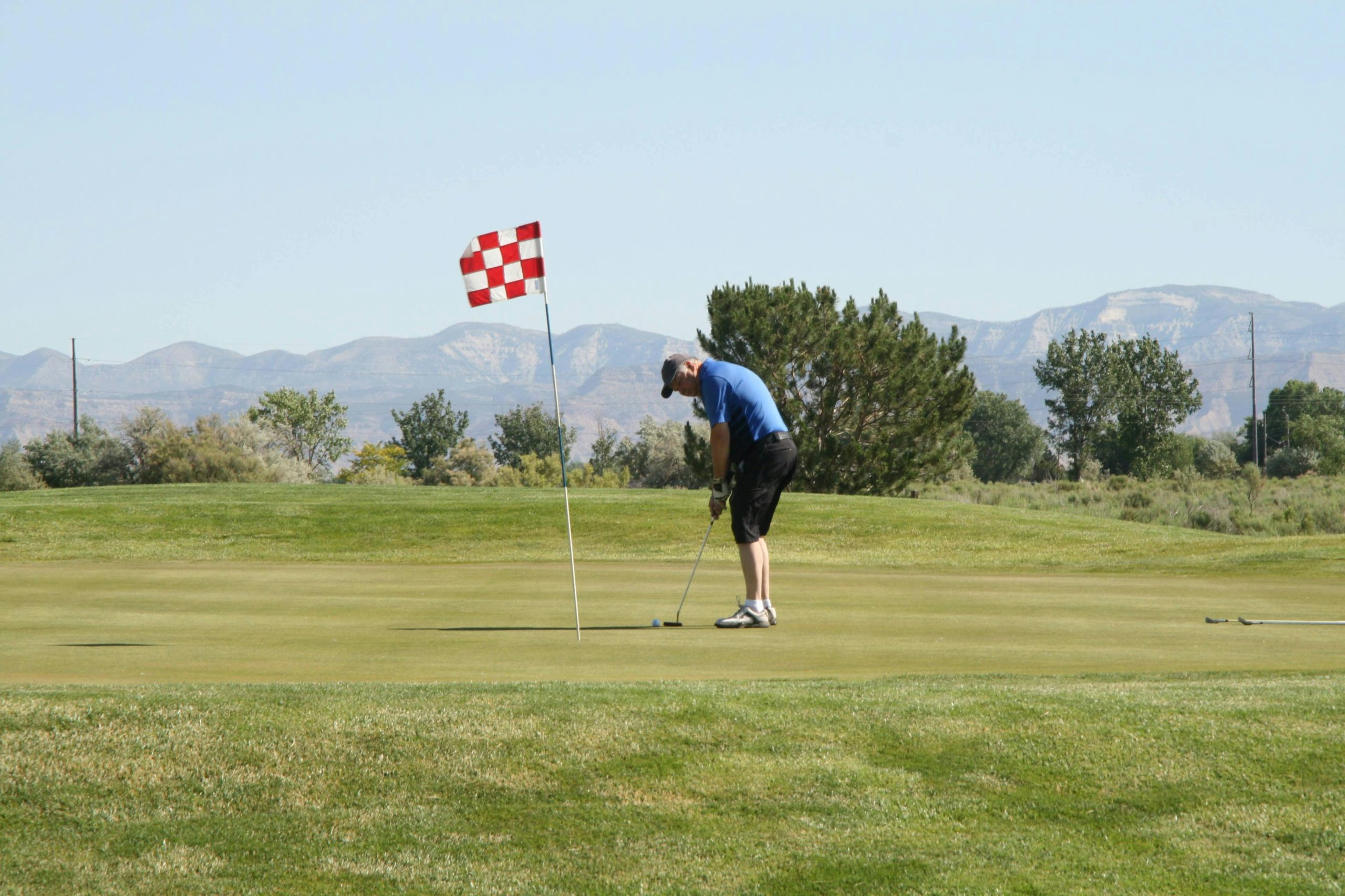 Golfeur puttant sur le green avec drapeau à carreaux rouges et blancs.