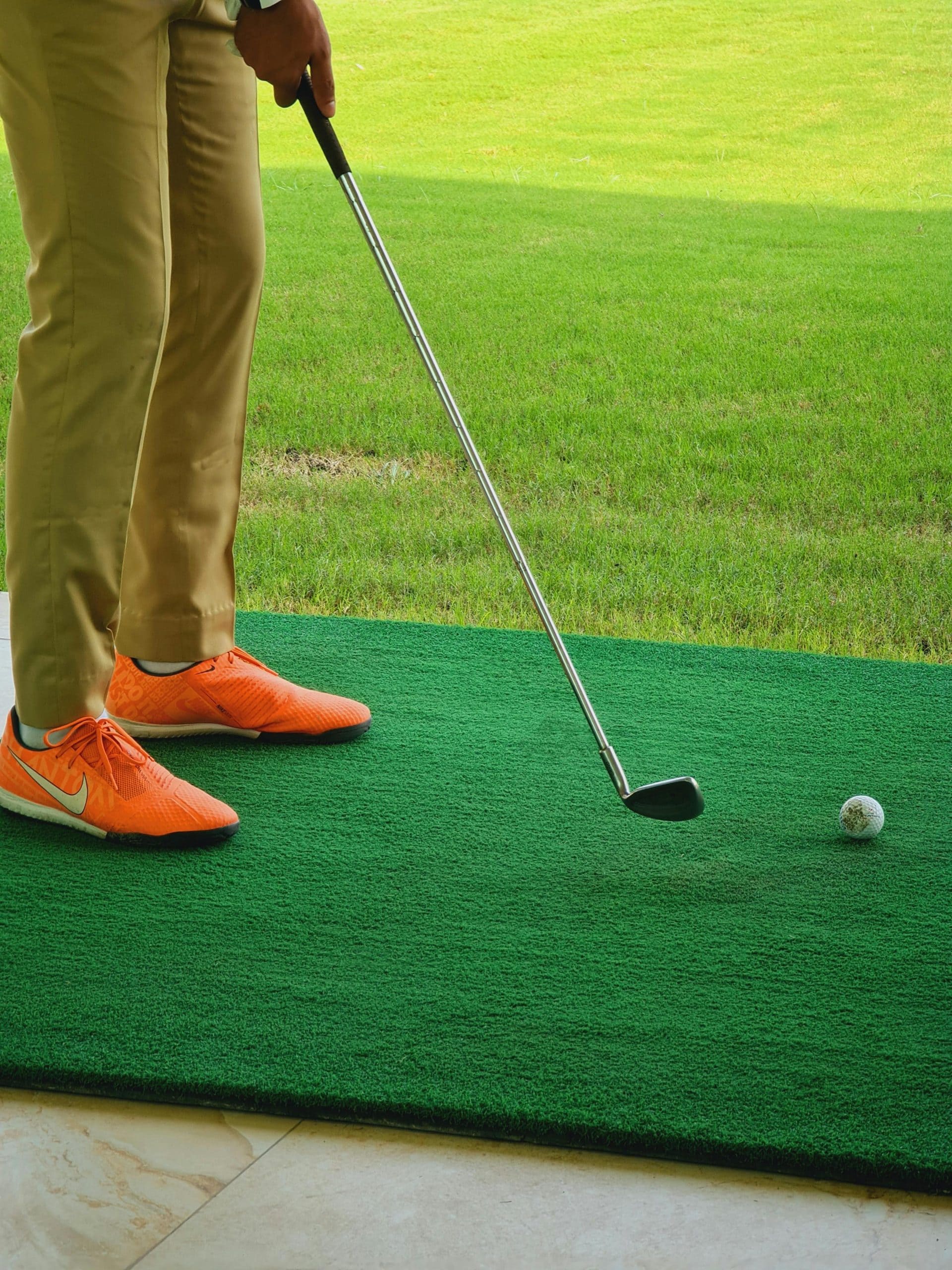 Joueur de golf en position avec club et balle sur tapis vert.
