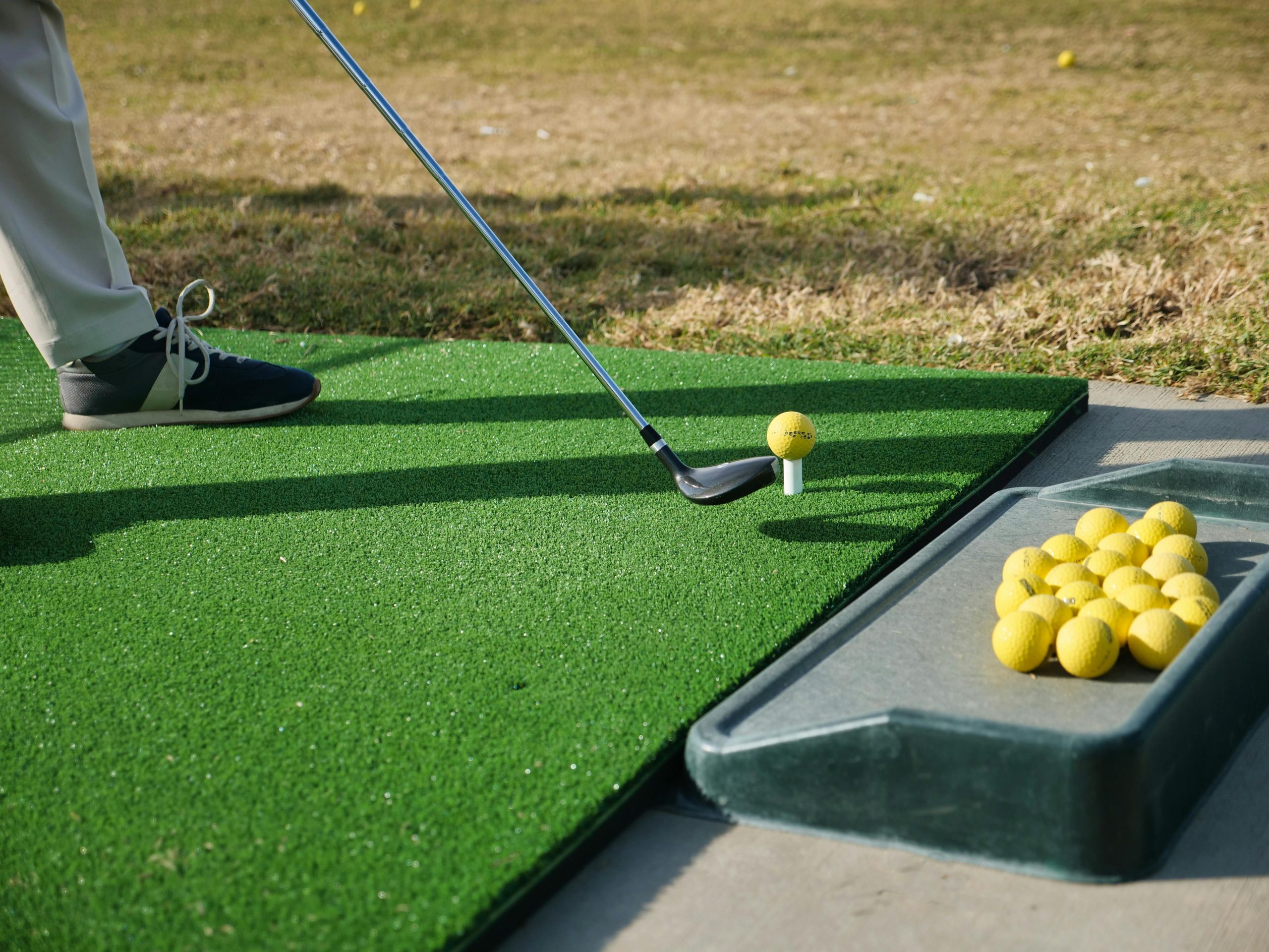 Golfeur prêt à frapper une balle jaune sur un tapis d'entraînement.