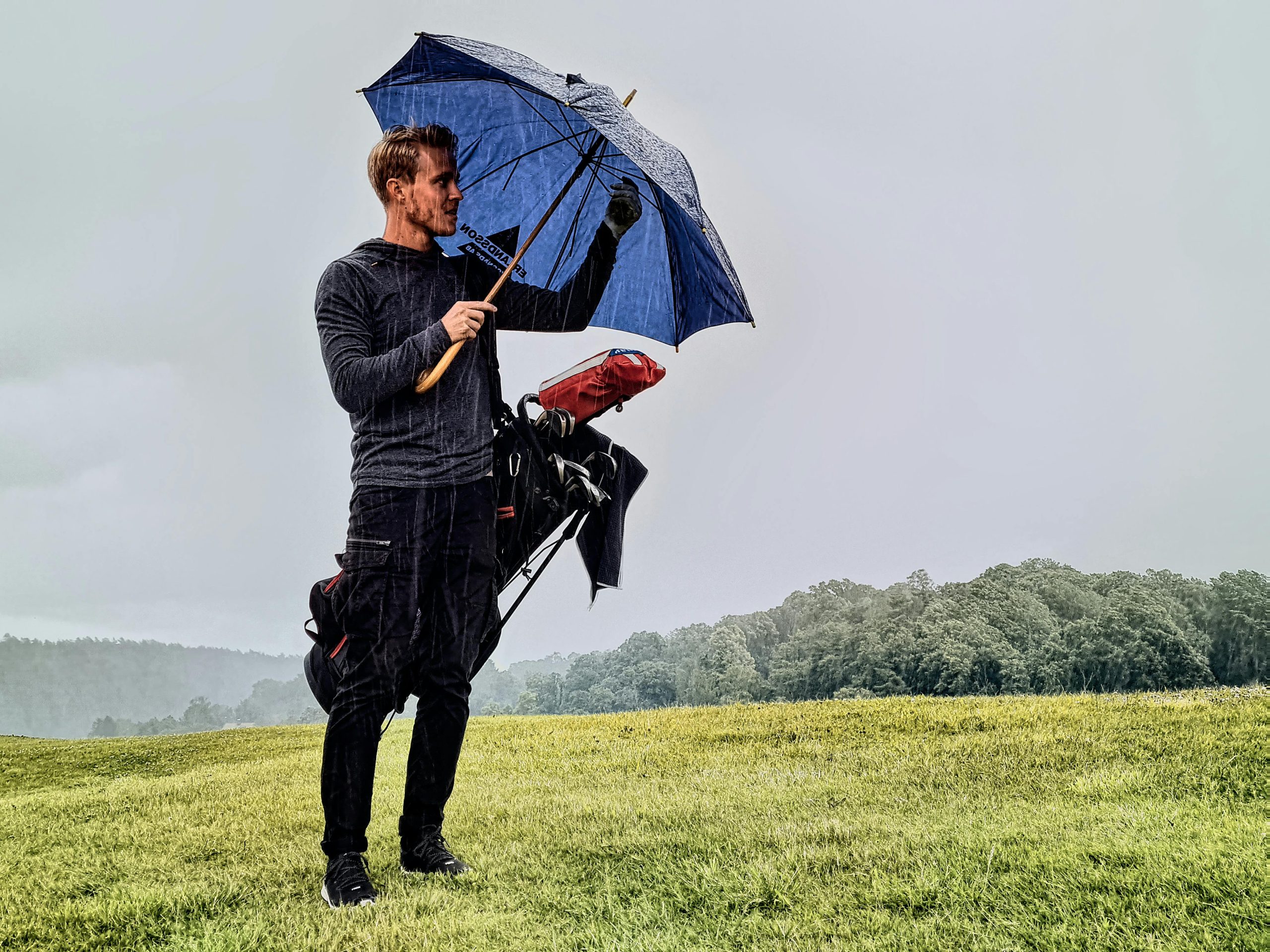 Homme avec parapluie sur un terrain de golf sous la pluie.