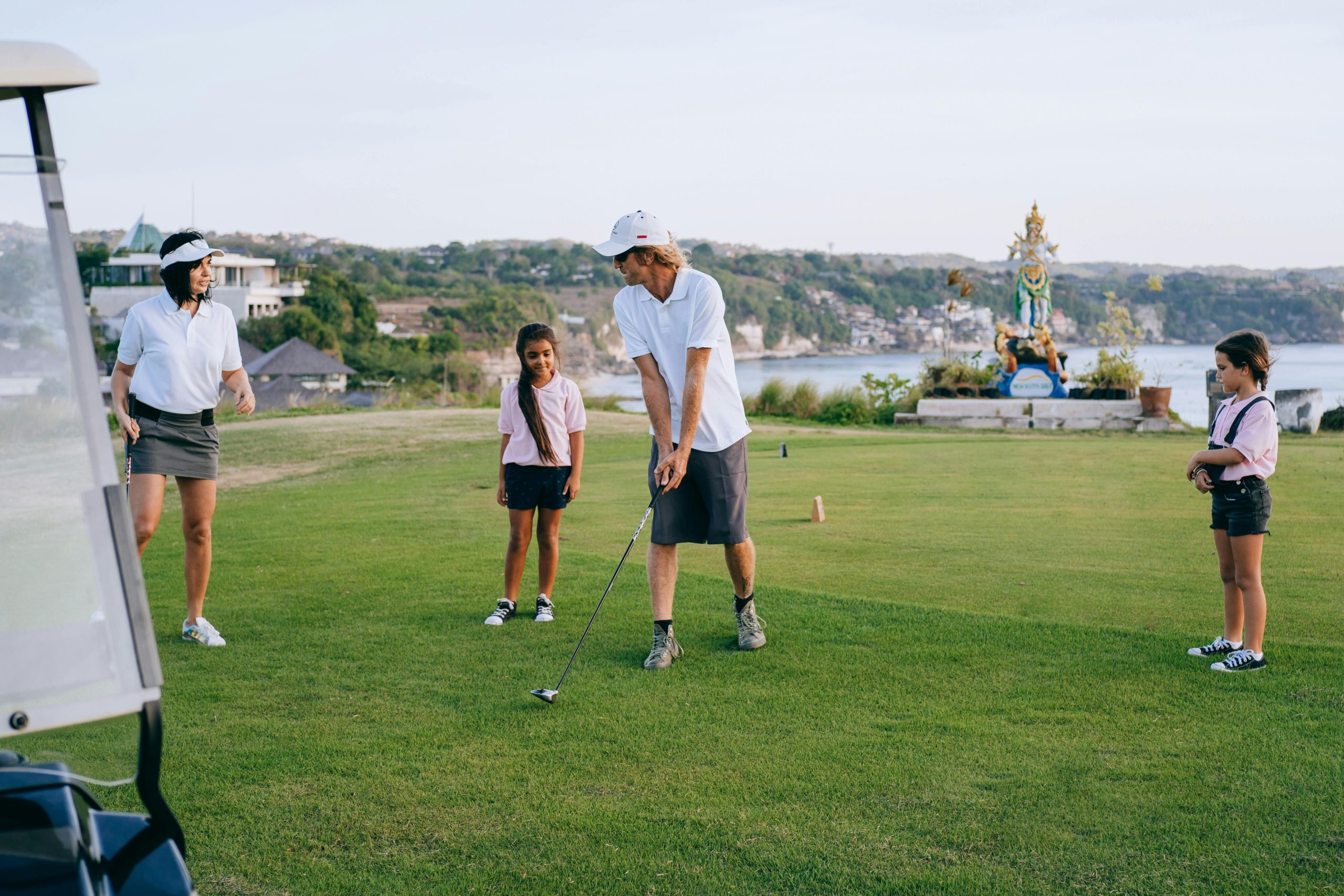 Un homme enseigne le golf à deux enfants sur un terrain verdoyant.