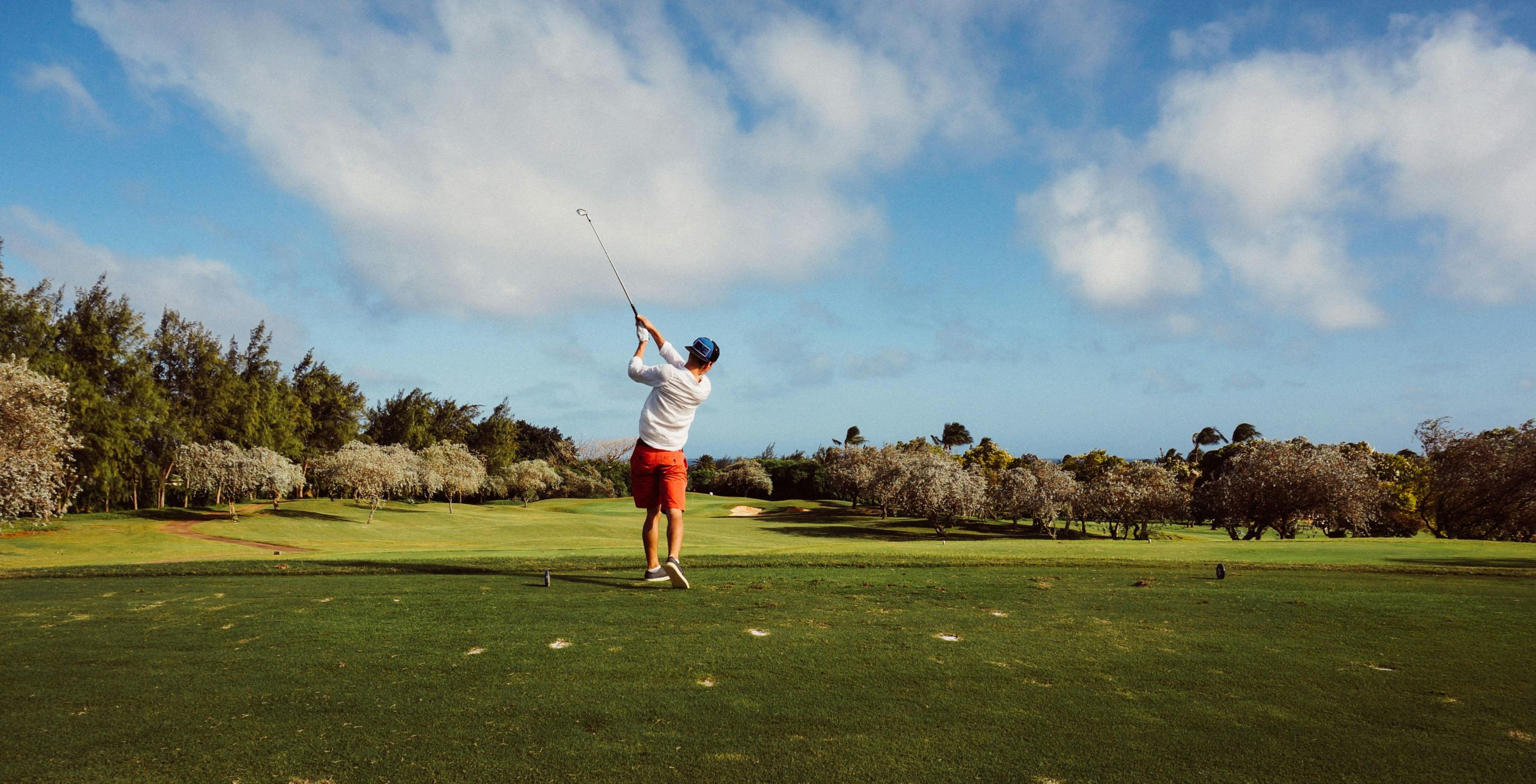 Golfeur en action sur un terrain verdoyant sous un ciel bleu.