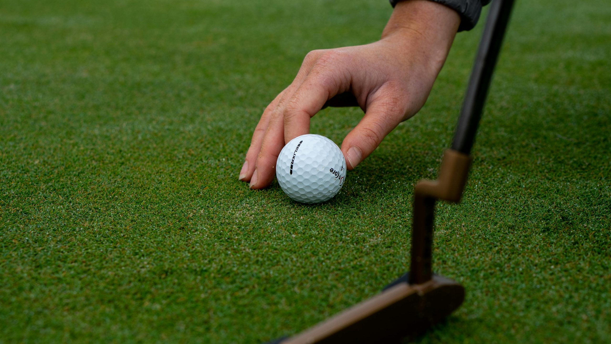 Main posant une balle de golf sur le green près d'un putter.