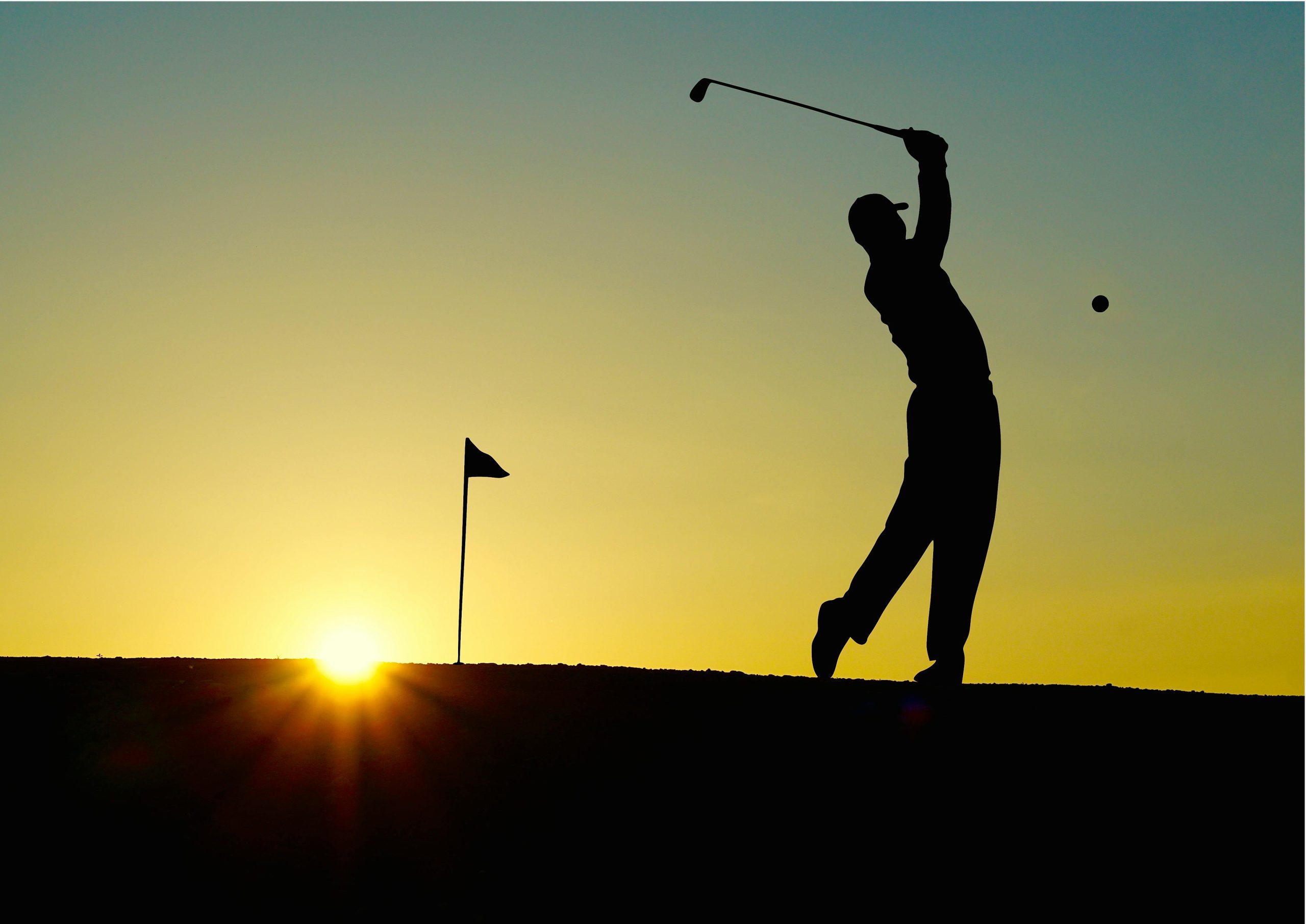 Golfeur frappant une balle au coucher du soleil, drapeau visible à l'horizon.