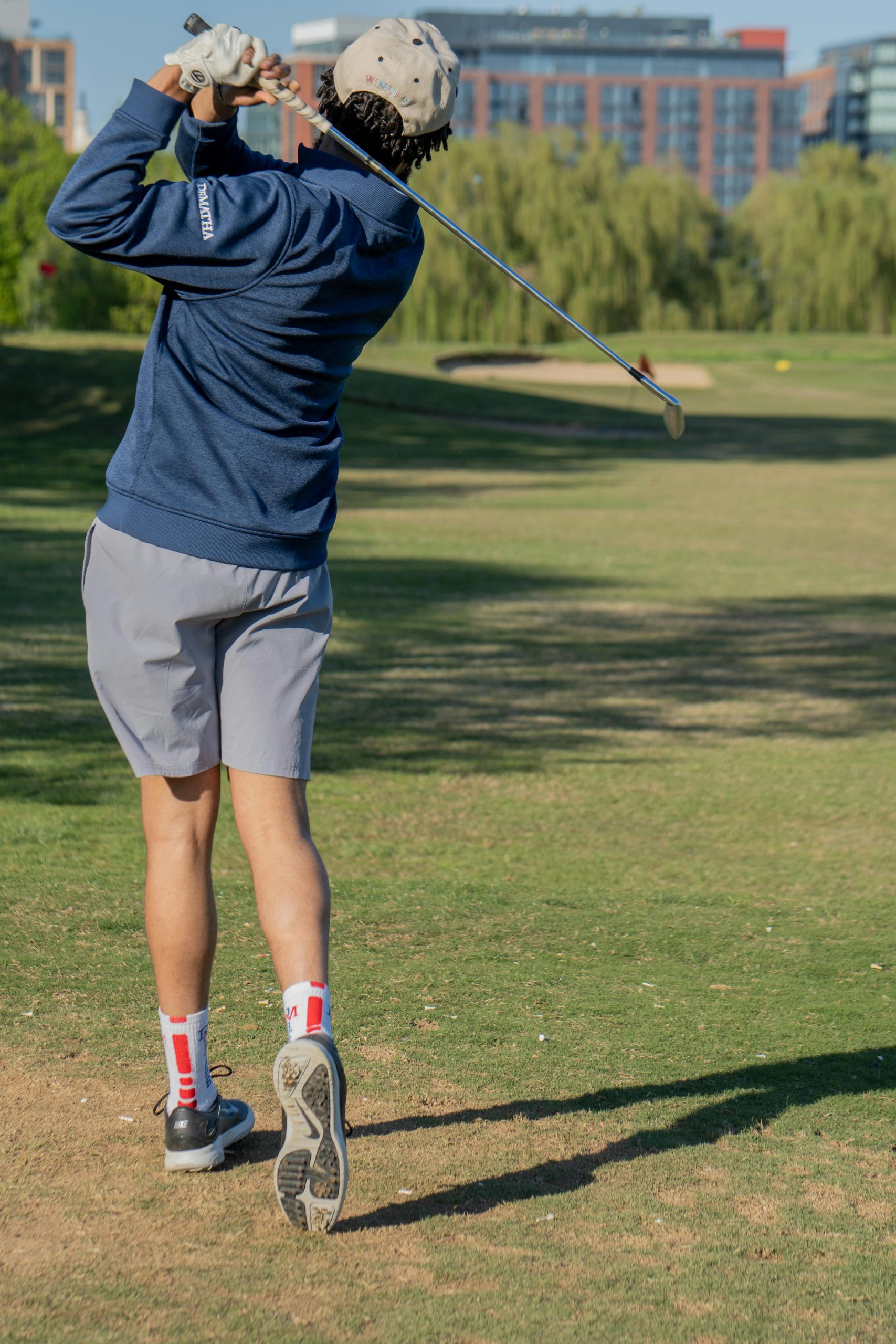 Golfeur en plein swing sur un parcours, bâtiments en arrière-plan.