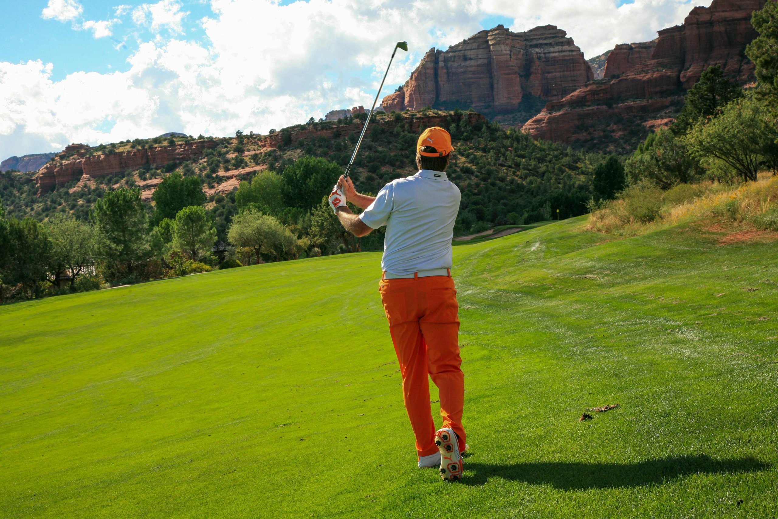 Golfeur en action sur un terrain verdoyant avec des montagnes en arrière-plan.