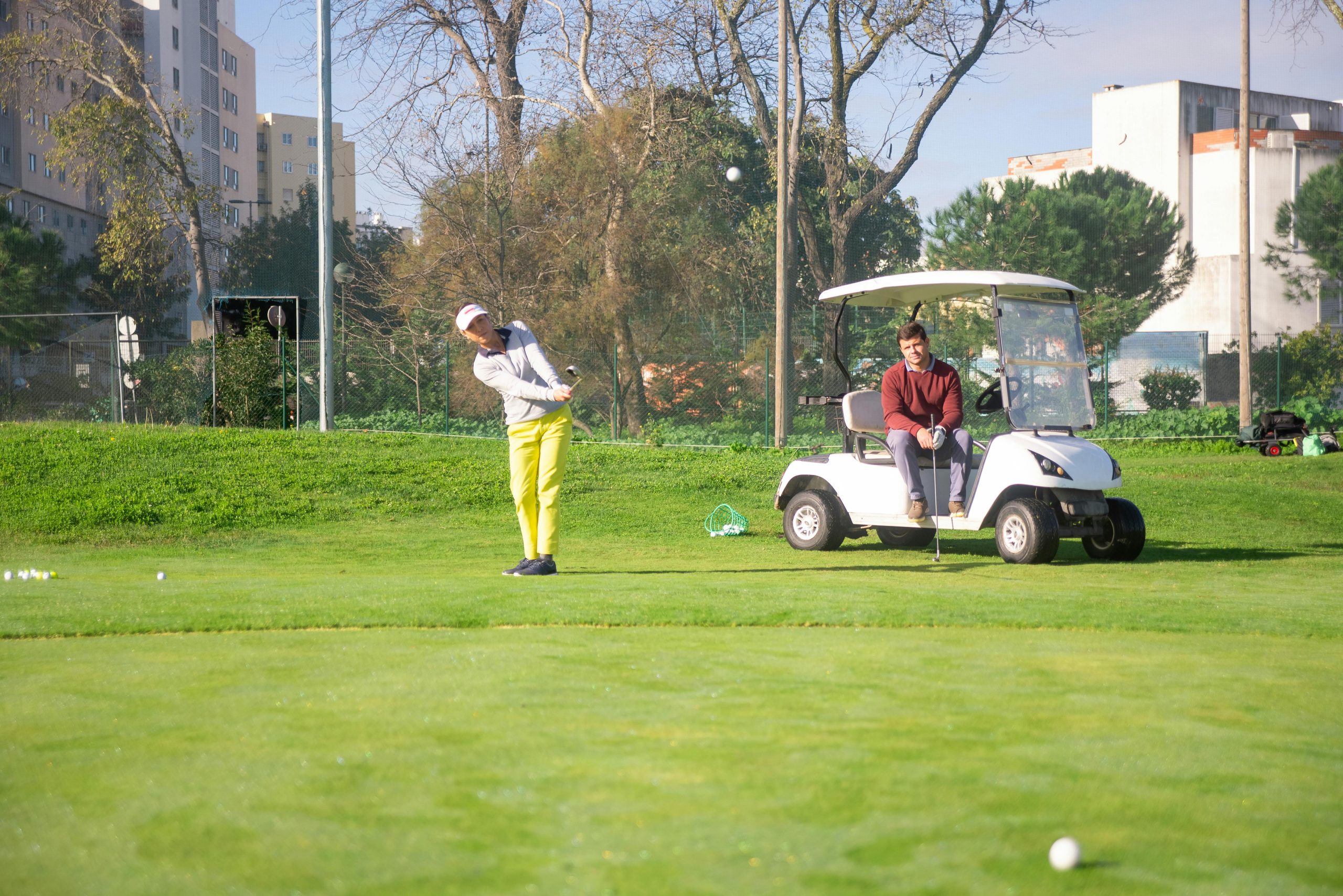 Golfeur frappant une balle près d'une voiturette sur un terrain de golf.