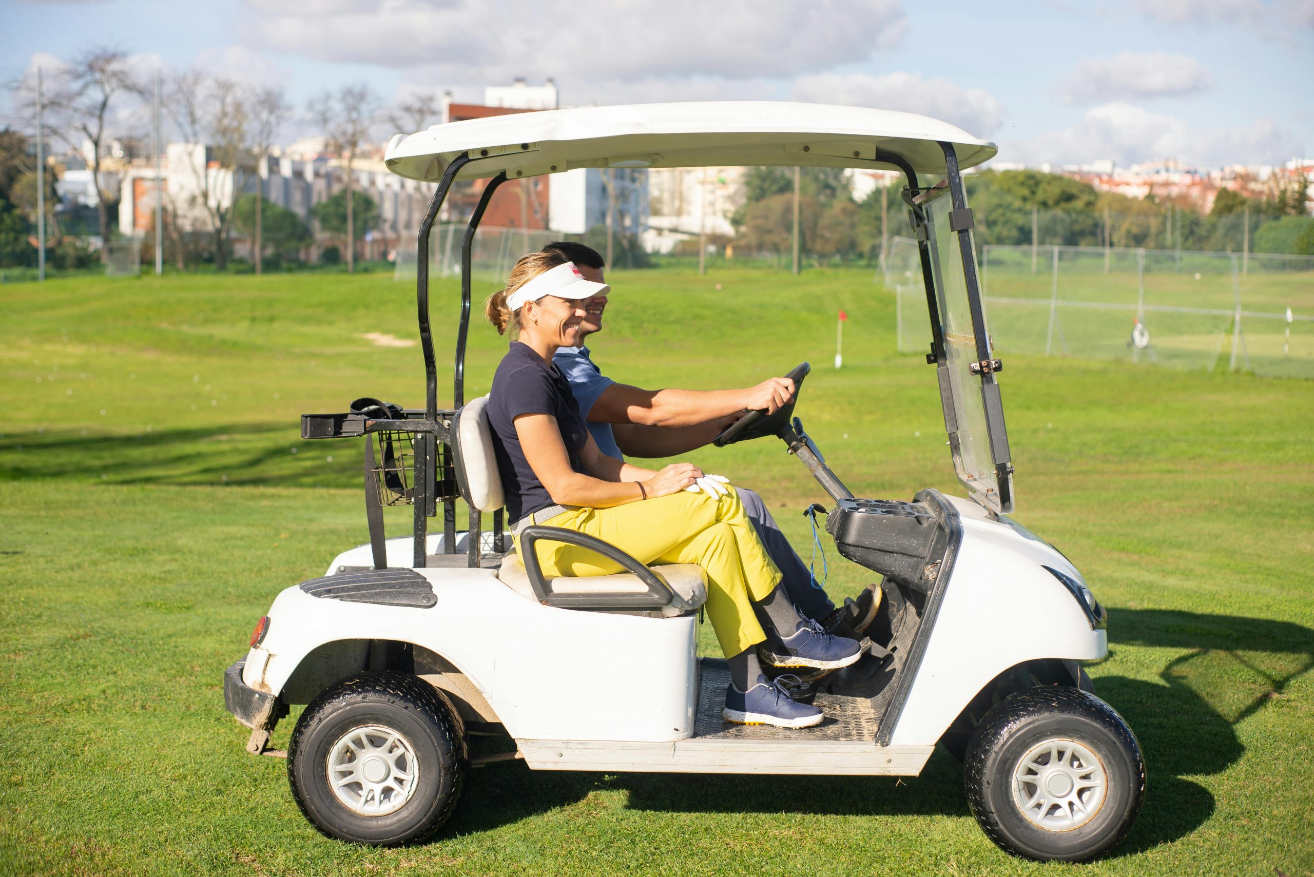 Deux personnes souriantes dans une voiturette de golf sur un parcours.