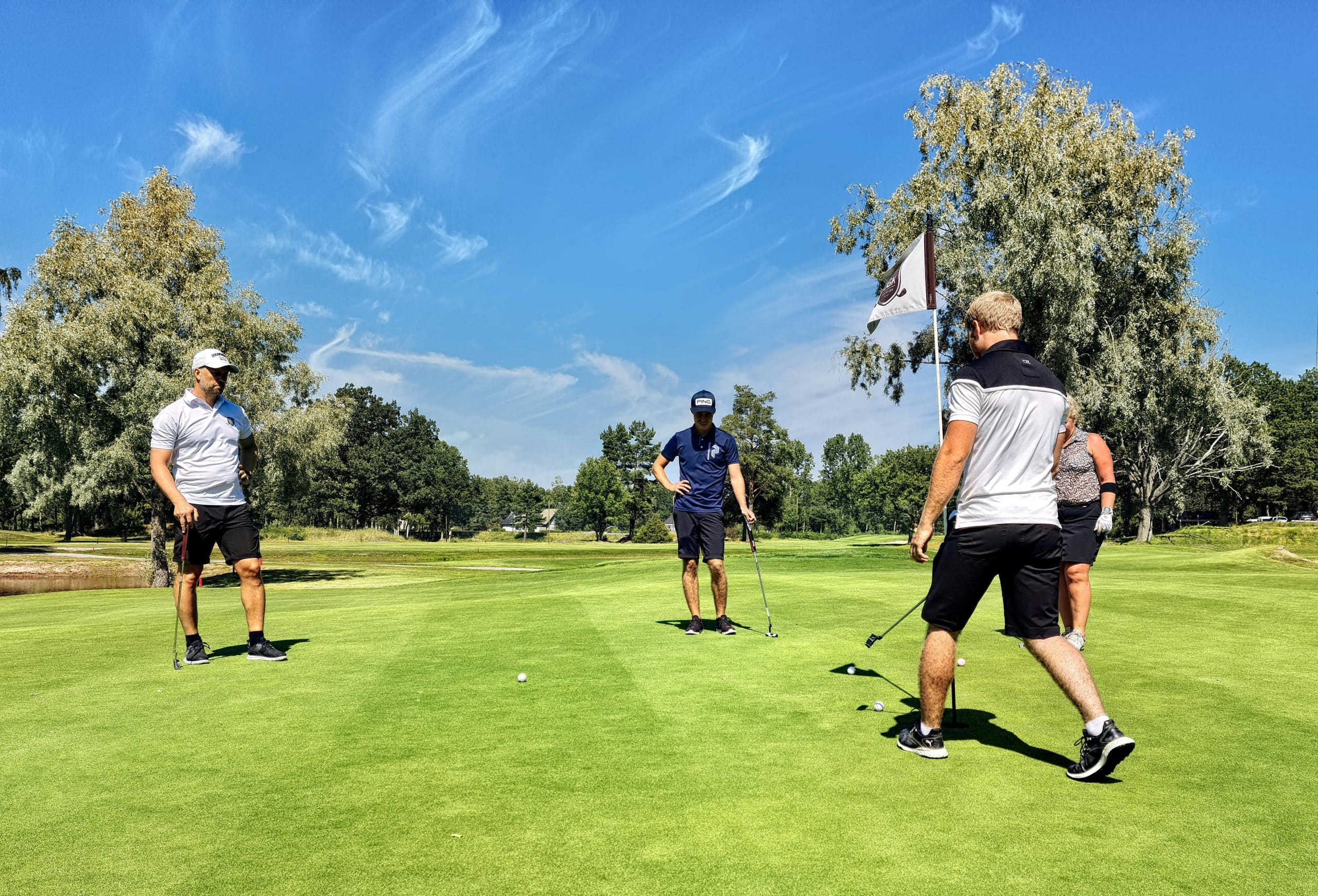 Quatre golfeurs sur un green, ciel bleu en arrière-plan.